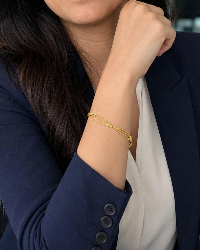 A woman with long dark hair sits in an office chair, wearing a navy blue blazer over a white top and a thin gold bracelet.